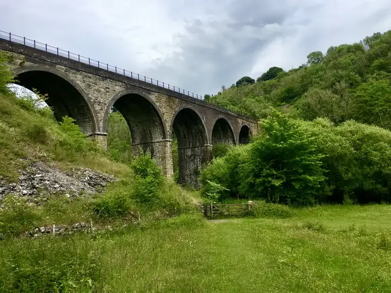 The Headstone Viaduct over Monsal Dale: five stone arches across a green valley under a grey sky, a field gate in the foreground.
